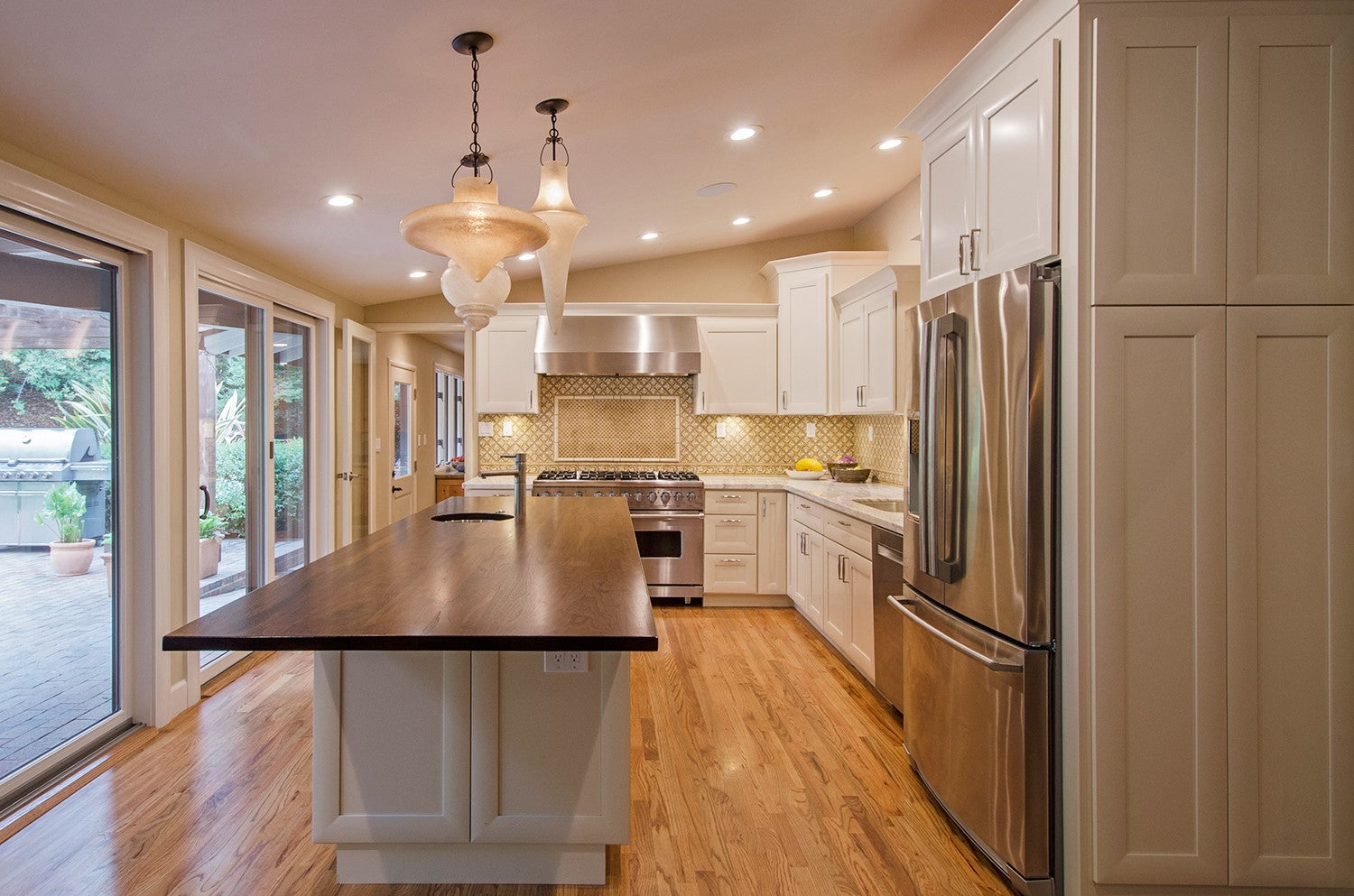 Remodeled Kitchen with White Painted Cabinets, Wood Countertop, Marble Countertop, Elaborate Backsplash and Assymetrical Pendant Lights